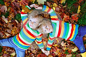 Two little twin kids boys lying in autumn leaves in colorful fashion clothing. Happy siblings having fun in autumn park