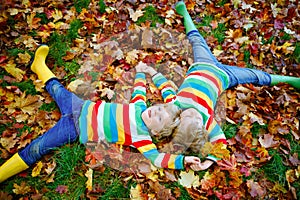 Two little twin kids boys lying in autumn leaves in colorful fashion clothing. Happy siblings having fun in autumn park