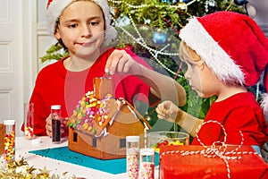 Two little young sibling boys glue chimney of gingerbread house