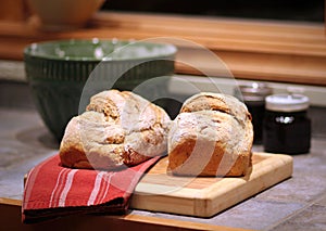 Two loaves of crusty homemade bread on cutting board in home kitchen.