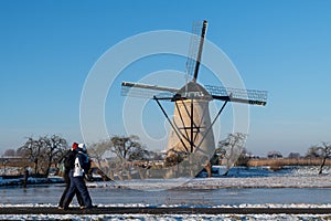 Two locals on a frozen windmill canal pathway at sunrise moment