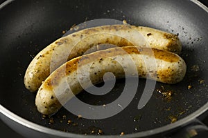 Two long bratwurst sausage grill with Italian mix herb in the hot non stick pan