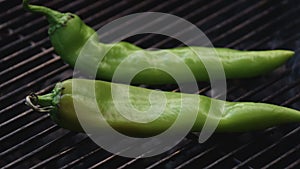 Two long chili peppers on a grill being roasted with some smoke