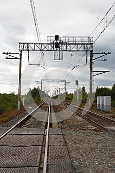 Two long and straight lines of railway rails with electric poles traffic lights signal lights electric supply boxes