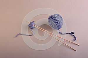 Two long wooden needles in a small ball of beautiful gray-blue thread next to a large ball of thread, on a harmonious soft beige