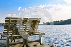 Two lounge chairs sit on a dock in summer beside a lake