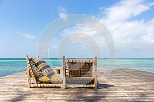 Two lounge chairs on wooden pier. Empty tropical resort. Pair of deck chairs with pillows on tropical beach. Luxury villa