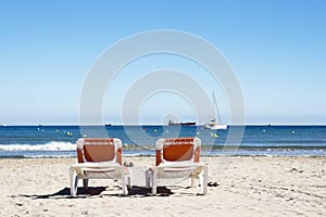 Two loungers on the beach with a view of yachts and ships.