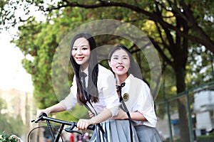 Two lovely Asian Chinese pretty girls wear student suit in school best friends smile laugh riding bike at playground