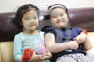 Two lovely baby girls are sitting on the sofa with dolls in their hands
