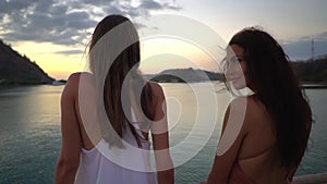 Two lovely brunette models are posing with their backs to the camera with sunset sky in the background in the ocean