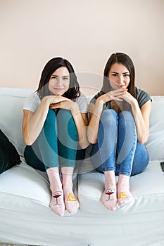 Two lovely girls are sitting on the couch looking at the camera.