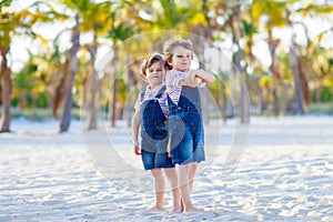 Two lovely little brothers sitting on sand on tropical beach, happy best friends, kids boys playing, friendship concept