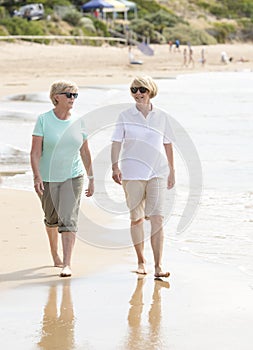 Two lovely senior mature retired women on their 60s having fun enjoying together happy walking on the beach smiling playful