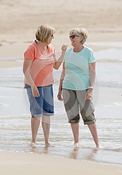 Two lovely senior mature retired women on their 60s having fun enjoying together happy walking on the beach smiling playful