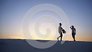 Two lovers of heart, guy and girls are having fun and running through hills of sandy desert on summer evening in open