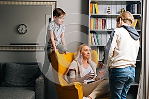 Two loving child son presenting to surprised mom gift box on Mothers Day in cozy living room. Concept of family holidays