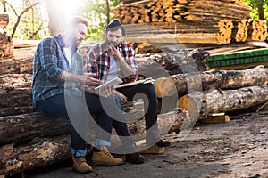 two lumberjacks sitting on logs with axe and using digital tablet