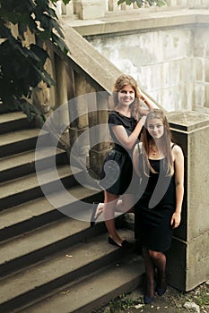 Two luxury gorgeous woman  in black dress posing, standing on old stairs and tree in city, classic gothic lady outfit