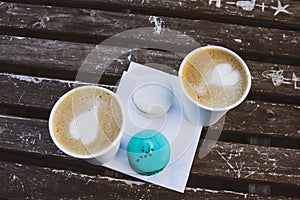 Two macaroons of mint and white, two coffee in paper cups, on a wooden vintage table.