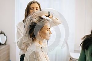 Two make-up artistes applies hair and makeup to the bride in dressing room. photo