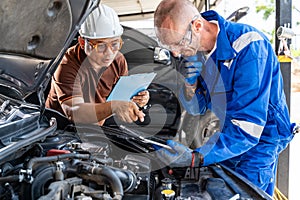 Two male auto mechanics working together on the car engine at their car repair garage