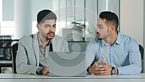 Two male colleagues employees cooperating in office talking working together at workplace, serious businessmen coworkers