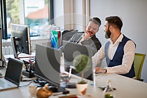 Two male colleagues gossip at work in open space office