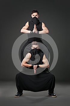 Two male dancers posing in ninja costumes on dark gray background.