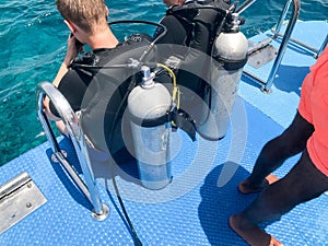 Two male divers in black diving waterproof suits with shiny metal aluminum canisters are preparing to dive from the boat to the bl