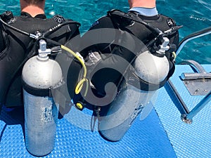 Two male divers in black diving waterproof suits with shiny metal aluminum canisters are preparing to dive from the boat to the bl