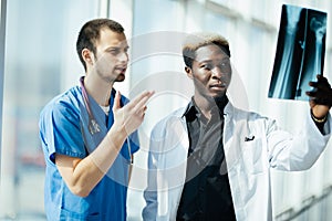 Two mixed race male doctors examining x-ray on modern office of hospital