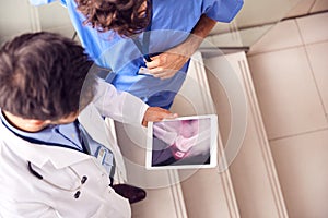 Two Male Doctors Having Informal Meeting In Modern Hospital Looking At X Ray On Digital Tablet