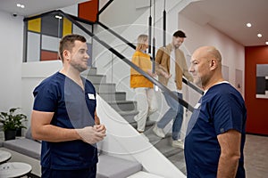 Two male doctors in uniform talking together at modern clinic hall