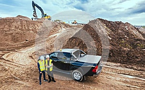 Two male engineers in overalls and white helmets stand near a special vehicle against the background of the construction