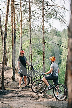 two male extreme cyclists in helmets with mountain bikes resting with sport bottles of water