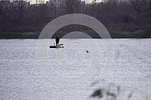 Two male fishermen in warm clothes on a boat, winter fishing on a river or lake. Photo through dry, brown reeds or grass