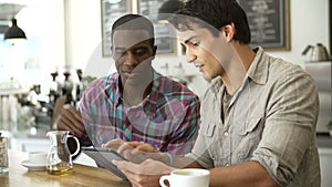 Two Male Friends In Coffee Shop Looking At Digital Tablet