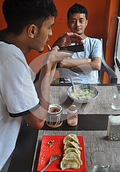 Two male friends enjoying fast food at the cafe with taking pictures of food with mobile phone