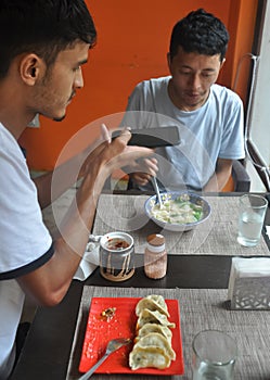 Two male friends enjoying fast food at the cafe with taking pictures of food with mobile phone