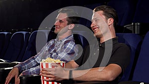 Two male friends laughing while watching comedies at the cinema