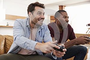 Two Male Friends Sitting On Sofa In Lounge Playing Video Game