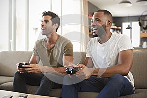 Two Male Friends Sitting On Sofa In Lounge Playing Video Game