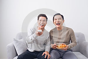 Two male friends watching football sitting on sofa at home