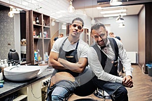 Two male haidressers and hairstylists sitting in barber shop.