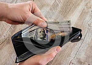 Two male hands holding a leather wallet with US Dollars cash inside