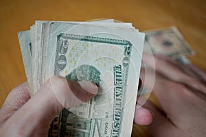 Two male hands holding a set of paper banknotes (American Dollars, USD) and giving the money on the wooden table