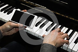 Two male hands on the piano with a smartphone. palms lie on the keys and play the keyboard instrument in a music school. student
