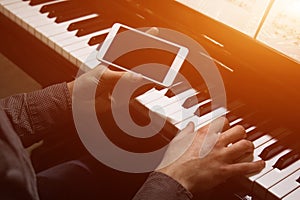 Two male hands on the piano with a smartphone. palms lie on the keys and play the keyboard instrument in a music school. student