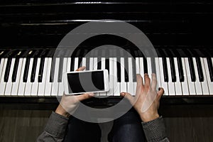 Two male hands on the piano with a smartphone. palms lie on the keys and play the keyboard instrument in a music school. student